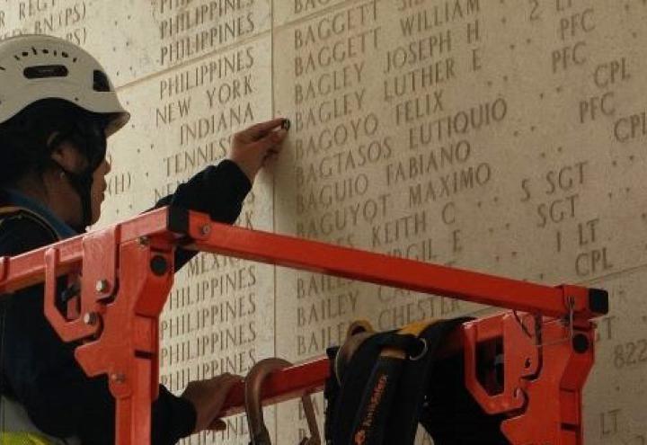 a staff member places a bronze rosette next to an engraved name on a stone wall.