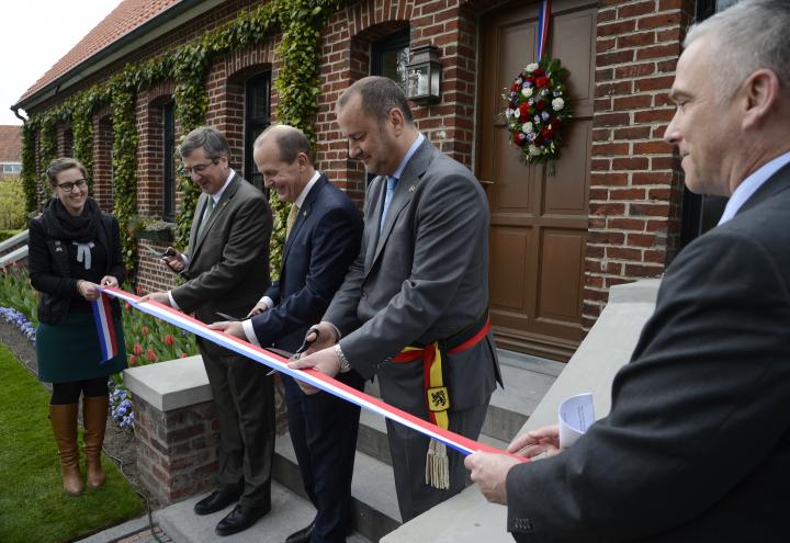 Three men in suits prepare to cut the ribbon at dedication ceremony. 