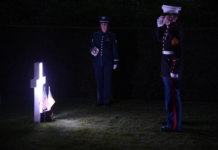 Light shines on a single headstones as two Marines salute. 