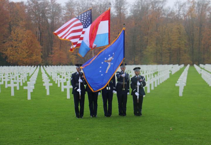 Honor Guard participants stand with firearms or flags in the plot area. 