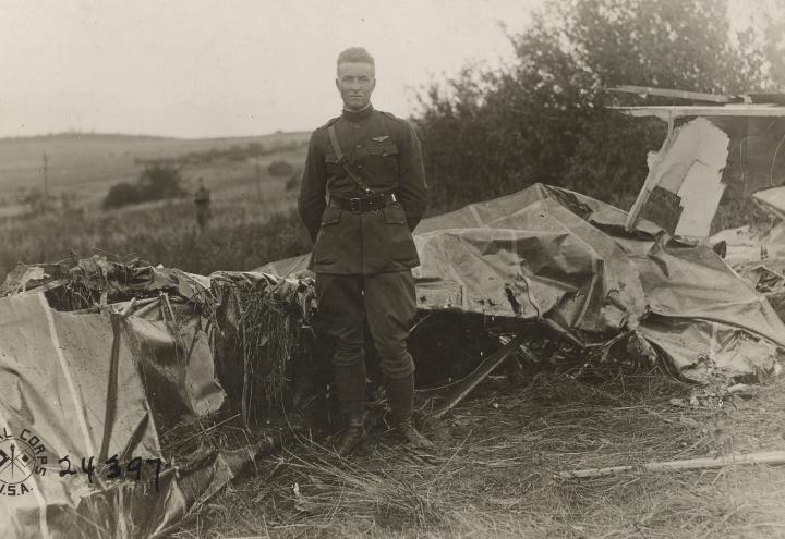 Historic photo showing man in uniform in front of destroyed plane. 