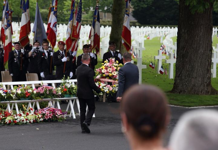 Two men carry a large floral wreath and prepare to lay it during the ceremony. 