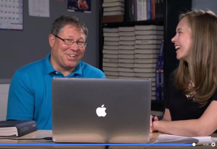 Man and woman sit in classroom with laptop in front of them. 