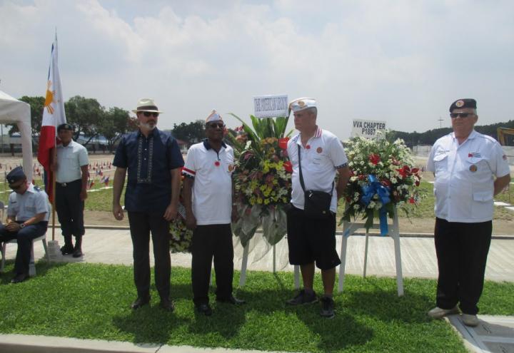 Men stand next to the stands holding the floral wreaths. 