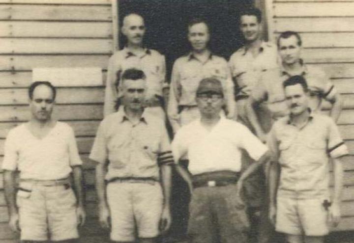 Historic photo of eight men standing in front of building.