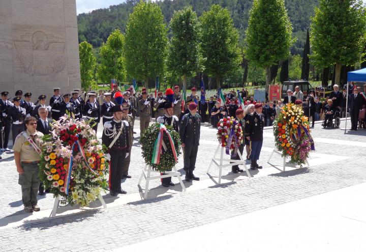 Large floral wreaths sit on stands next to the participants that laid the wreaths. 