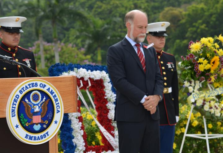 Ambassador Farrar stands next to the podium. 