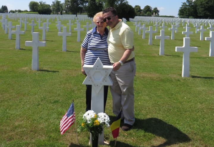 Woman and man stand next to each other behind a Star of David headstone. 