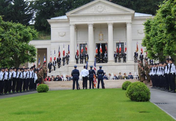 Flag bearers and men and women in uniform stand in front of the memorial building during the ceremony. 