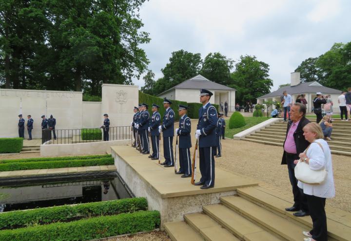 Men and women in uniform stand with weapons in front of them. 