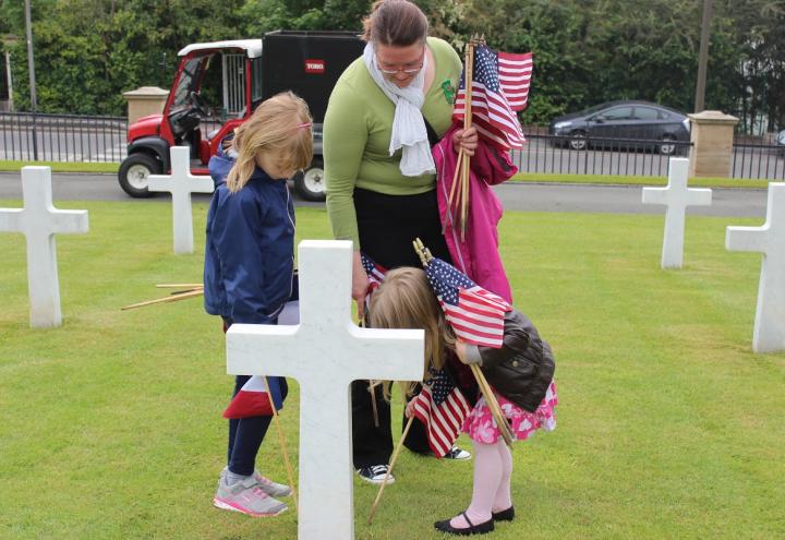 A woman and two children help to place the American and French flags in front of a headstone. 