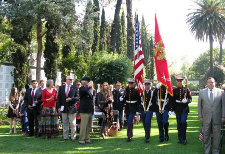 Men and women in uniform march with flags or firearms as part of the Honor Guard.