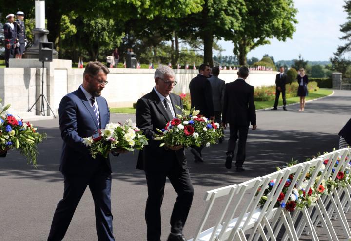 Two men carry floral wreaths to be laid. 