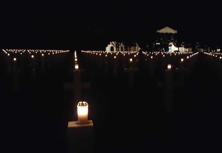 Candles on top of headstones burn bright int he darkness.