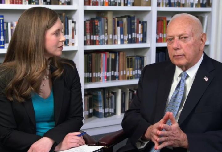 Woman and man sitting in chairs in front of a bookshelf. 