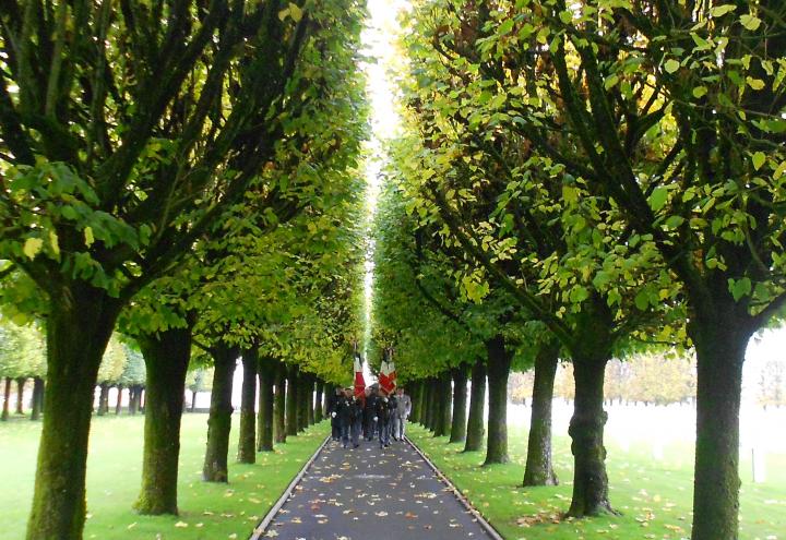 Men with flags march down a path in the middle of the cemetery.