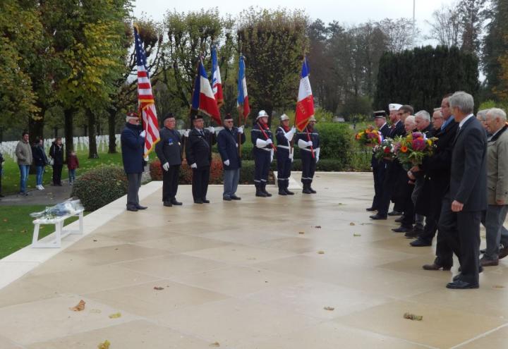 Men in uniforms or suits carry floral wreaths for placement. 