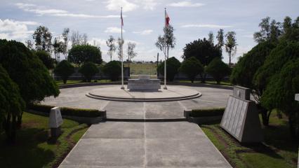 A distant view of the Cabanatuan American Memorial shows the entire plaza including a concrete pathway and two flags poles.