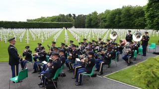 Men and women in uniform sit while they play their instruments. 