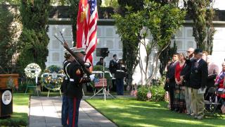 Men and women in uniform march with flags or firearms as part of the Honor Guard.