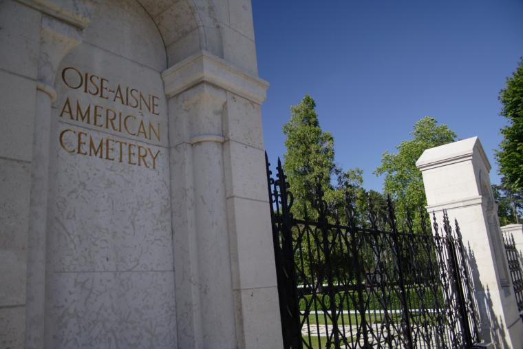 The entrance gate includes a stone column with the cemetery name engraved on it.