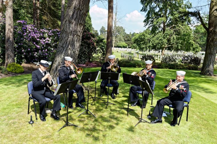 Men and women in uniform play their instruments while sitting. 