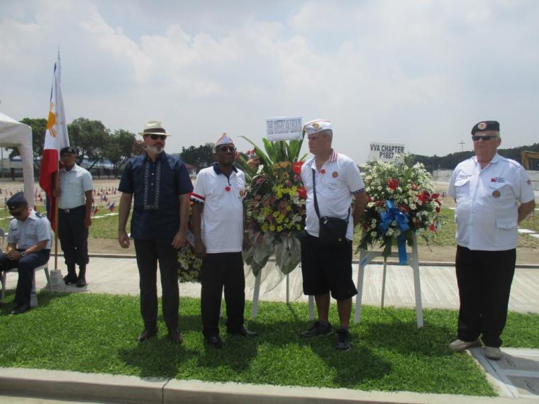 Men stand next to the stands holding the floral wreaths. 