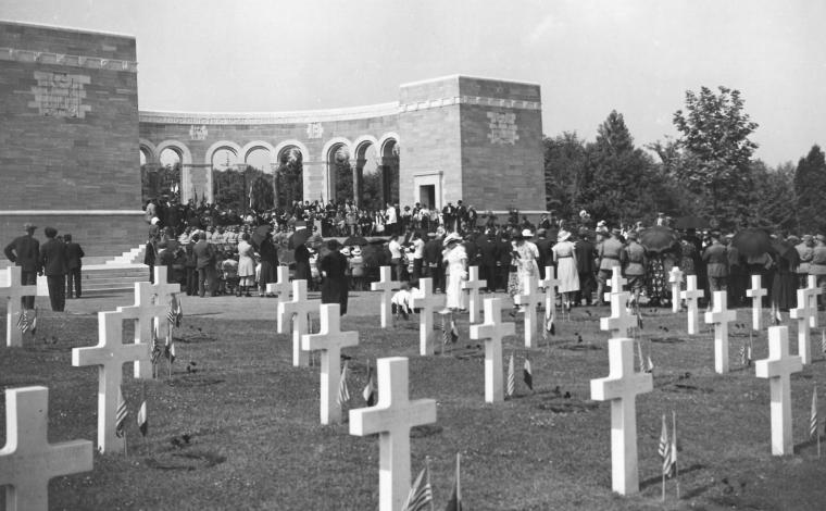 Historic photo shows headstones with flags and a crowd gathered in the memorial area. 