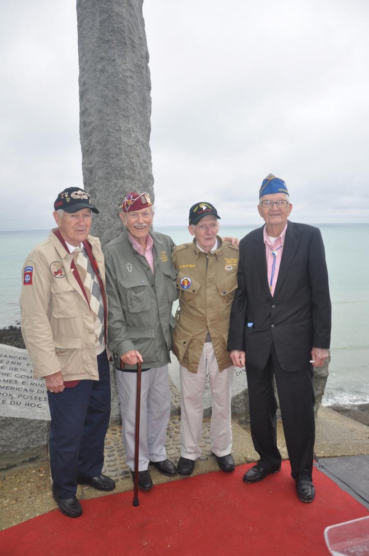 Four World War II veterans stand in front of the Ranger Monument at Pointe du Hoc.